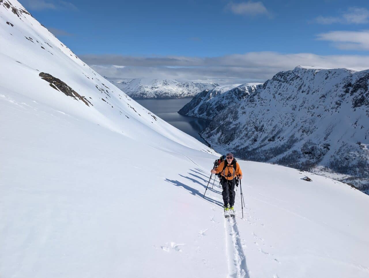 Skieur en montée au-dessus d’un fjord dans le Finnmark en Norvège avec neige fraîche en ski de randonnée