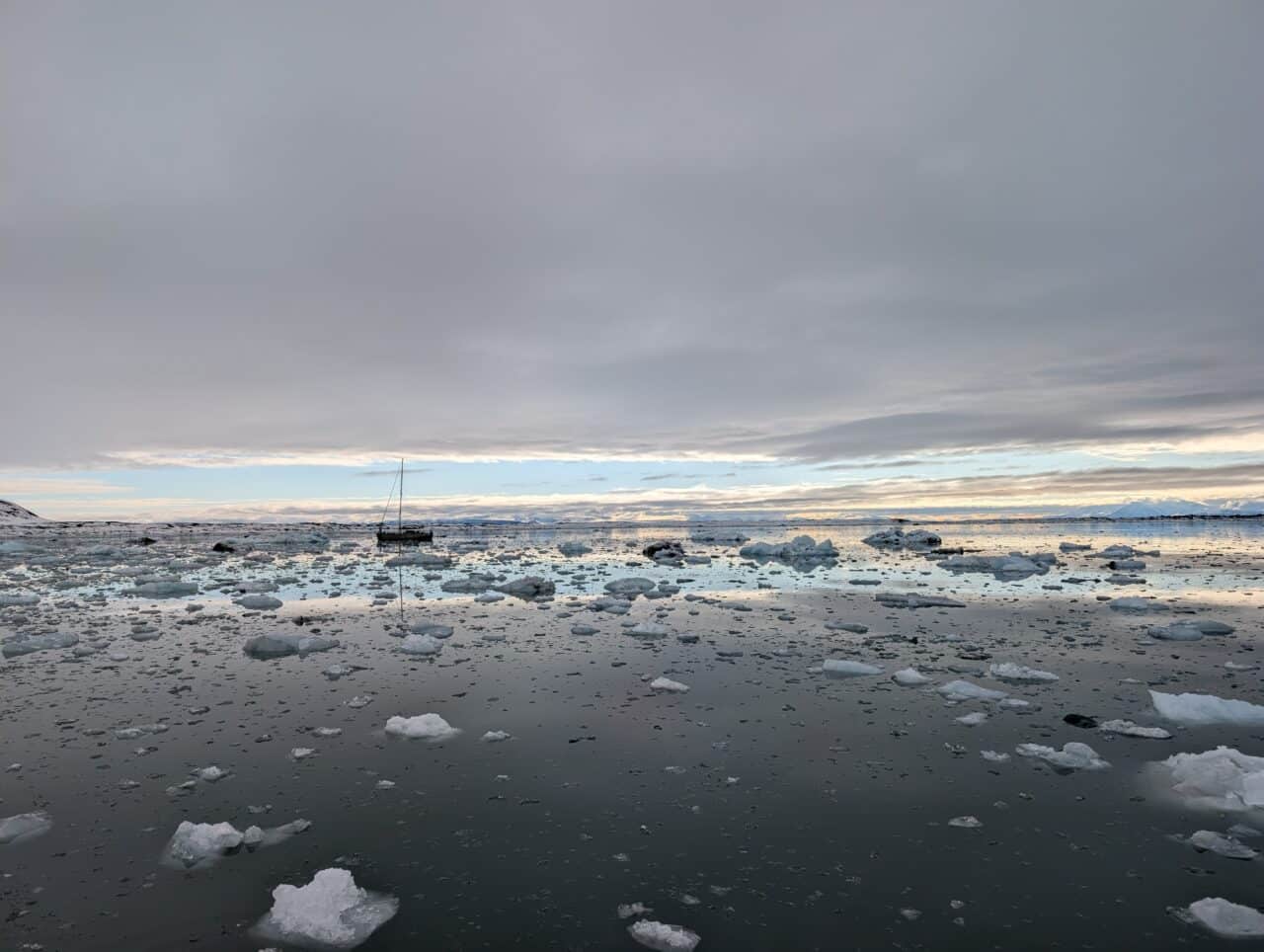 Voilier naviguant parmi les glaçons dans un fjord du Svalbard sous le soleil de minuit