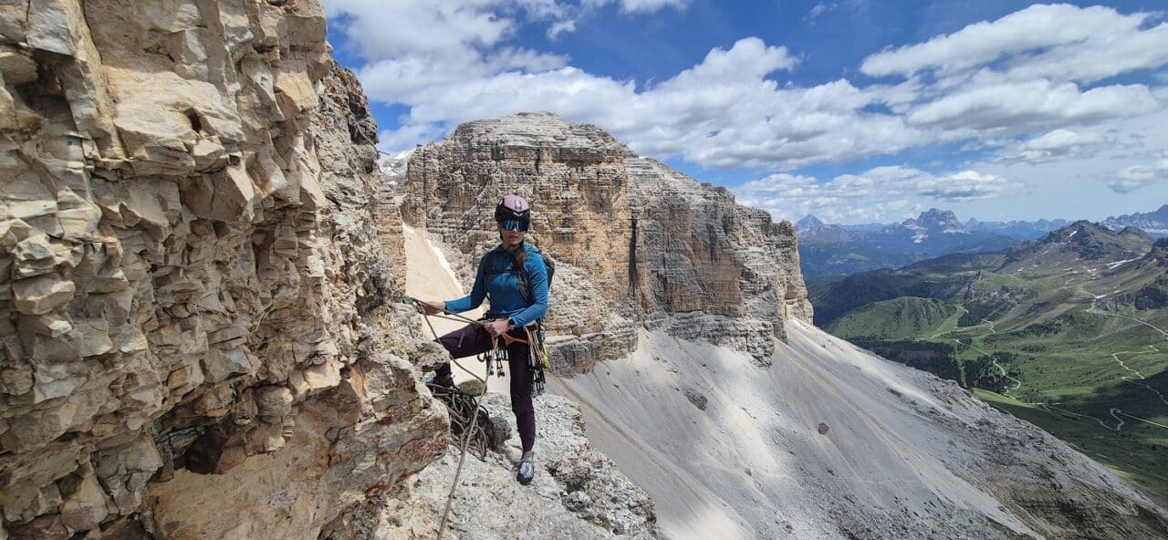 Grimpeur évoluant dans la voie Gross-Momoli sur les parois du Sass Pordoi, au cœur des Dolomites italiennes, avec une vue spectaculaire sur les sommets environnants.