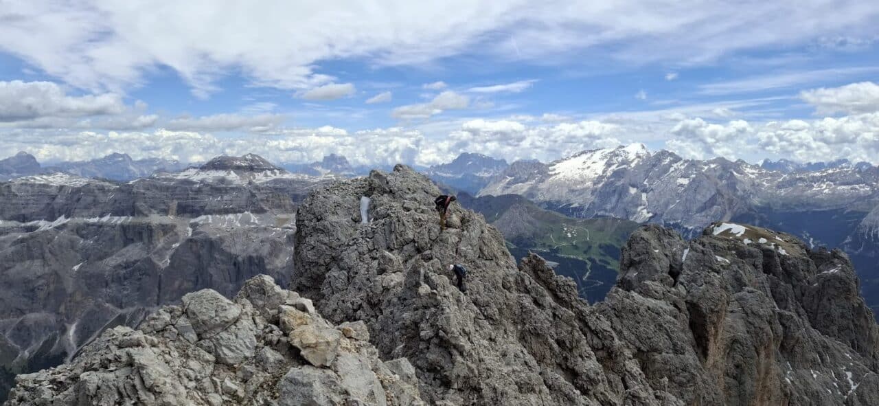 Alpiniste progressant sur l'arête finale du Sassolungo dans les Dolomites, avec une vue spectaculaire sur le massif du Sella et les montagnes environnantes.